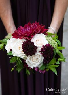 
                    
                        Bridesmaids carry colorful bouquets of white roses and deep purple dahlias backed with bright green leaves.
                    
                