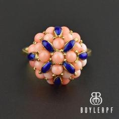 A fabulous fanciful feminine Italian ring features a profusion of hand-carved pink salmon colored coral beads with deep cobalt blue enamel leaves. An elaborate 18K yellow gold gallery supports all the gemstones to make this impressive breathtaking cocktail ring a singular sensation!