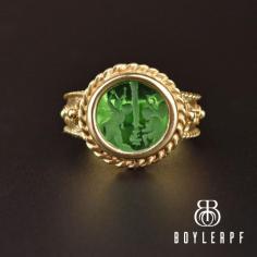 A stately neo-classic hand-carved Roman scene emerald quartz intaglio is the focal point of this masterfully crafted vintage ring rendered in a 14K yellow gold. The mythological cameo sports figures dancing with one a woman and child. The intaglio, which was used as a wax seal stamp, is inset an elaborately detailed frame with applied wirework shoulders and a decorated back band.