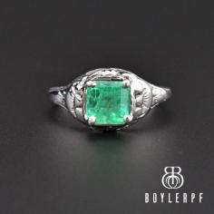 Beautiful emerald cut 1.10 carat natural emerald glows from this vintage Art Deco solitaire engagement ring handcrafted in 18K white gold. A detailed filigree white gold mounting cascades down the shoulders and into the band. 